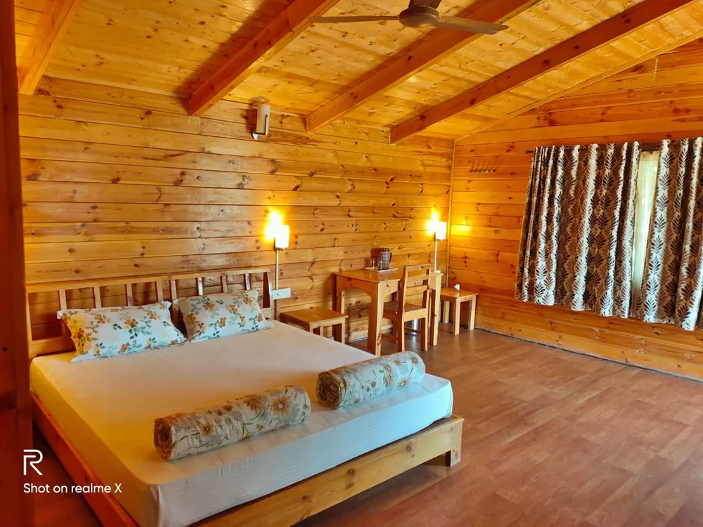 King-size bed with floral cushions and bolsters in the pine-panelled Superior King Room with Loft at Labdhi Resorts, under a vaulted timber ceiling
