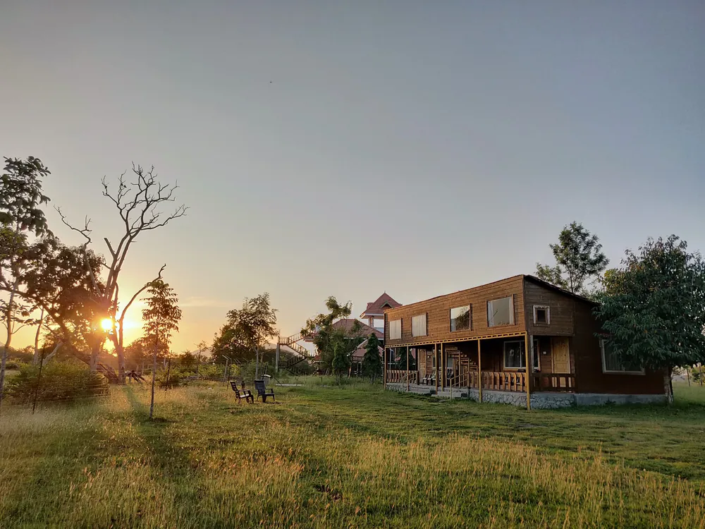 The sun setting behind trees across the grounds and a timber loft cottage at Labdhi Resorts