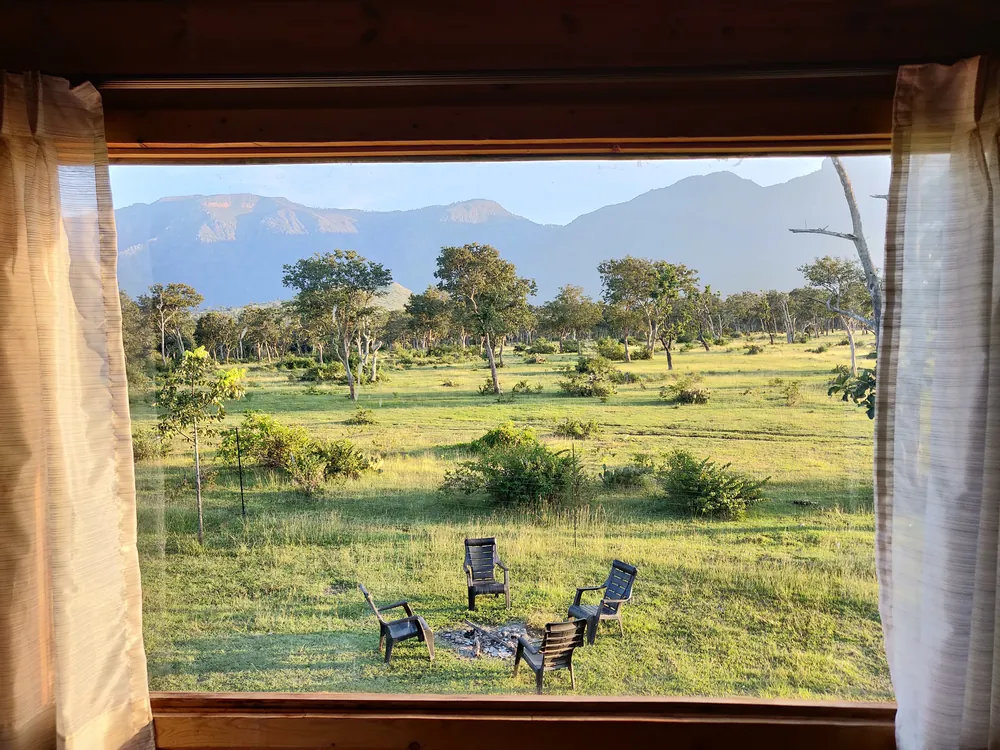 Picture window in the Superior King Room with Loft at Labdhi Resorts framing the lawn, the fire pit and the Nilgiri hills